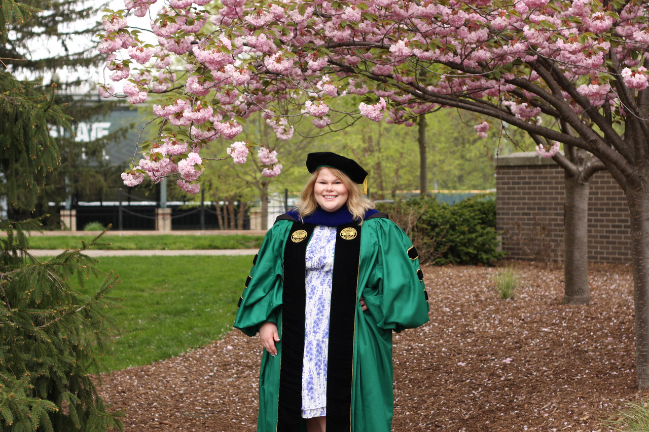 Sarah in graduation gown by flowering trees