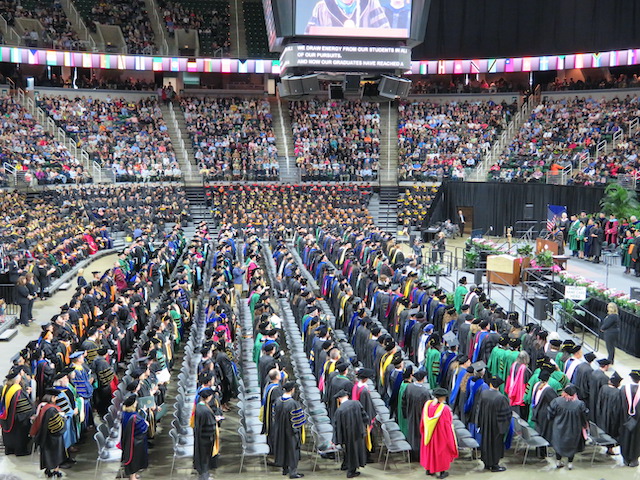 Advanced Degree Ceremony at the Breslin Center - graduates and faculty in hoods and gowns with the crowd in the arena.